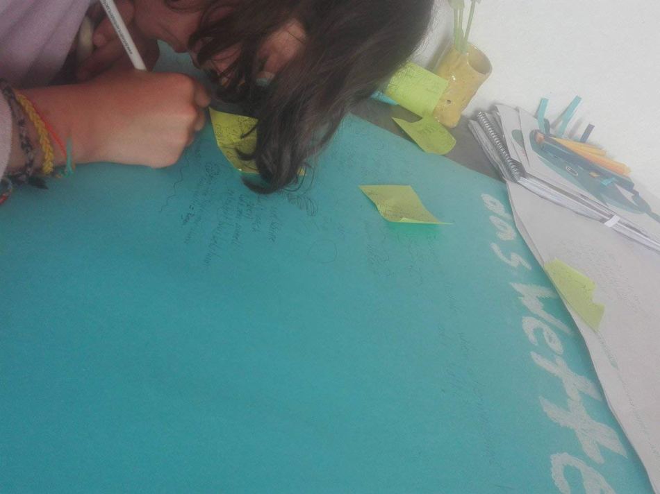 Antonia am Tisch über das blaue Plakat gebeugt konturiert am Schreiben